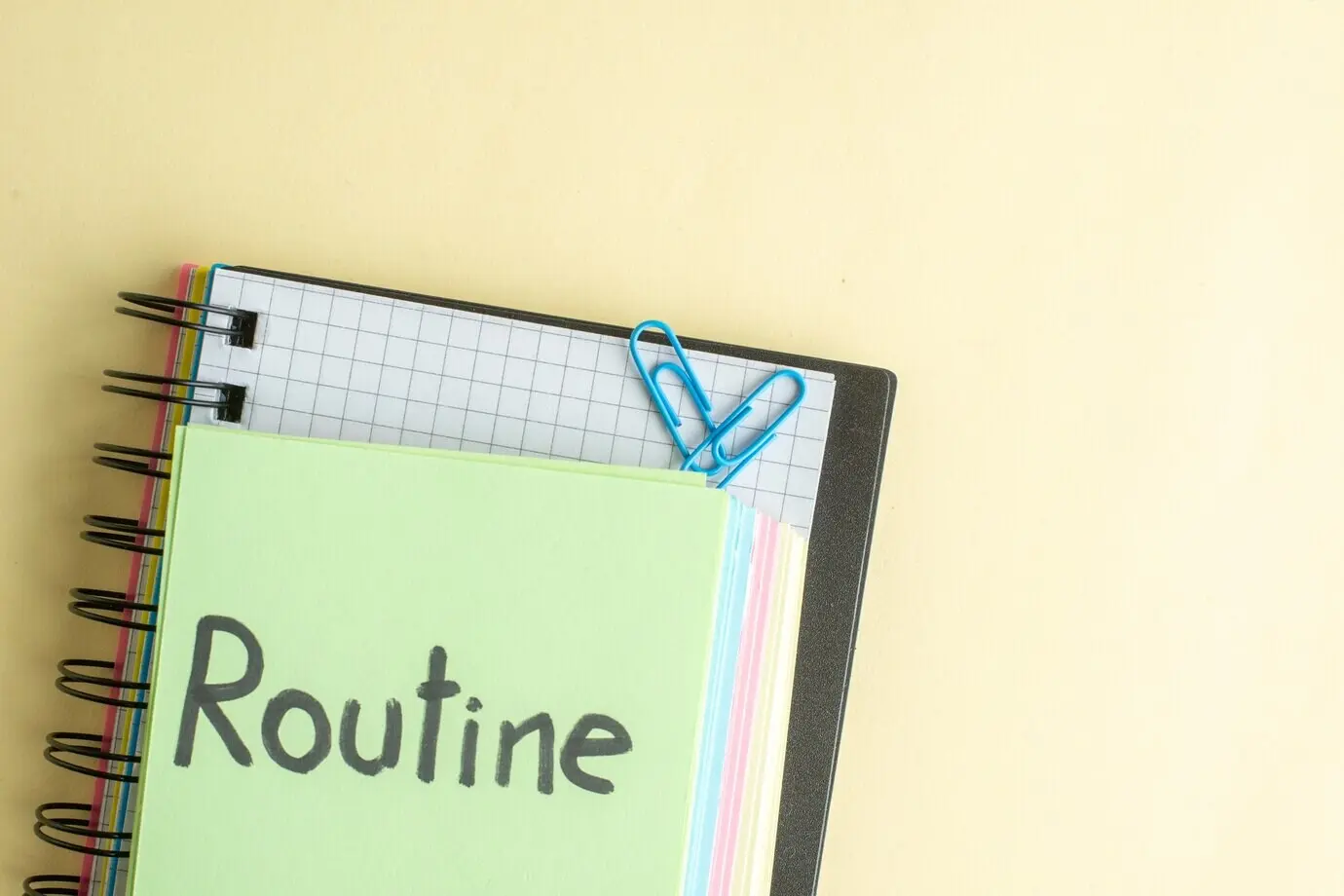 Top view of a routine written note with colorful paper notes on a light background, including a copybook, notepad, and pen, related to work, business, money, office, school, bank, and job.